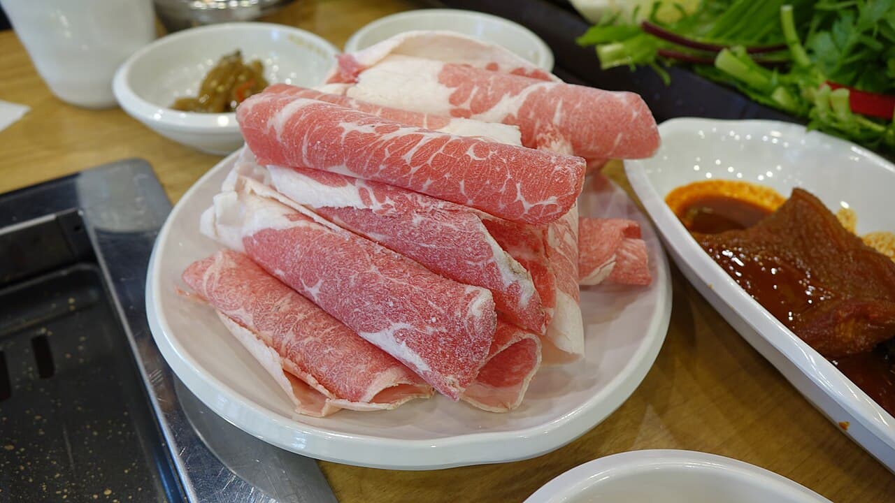 Thin-sliced and rolled chadolbagi beef brisket on a white plate at a Korean BBQ restaurant