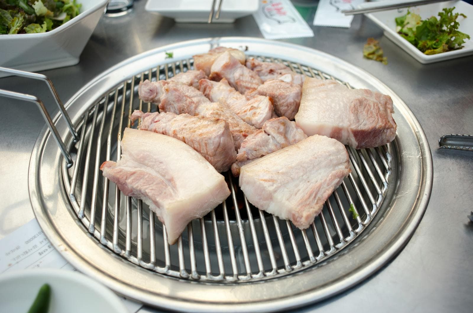 Thick chunks of raw ogyeopsal pork belly with skin on a Korean BBQ grill grate