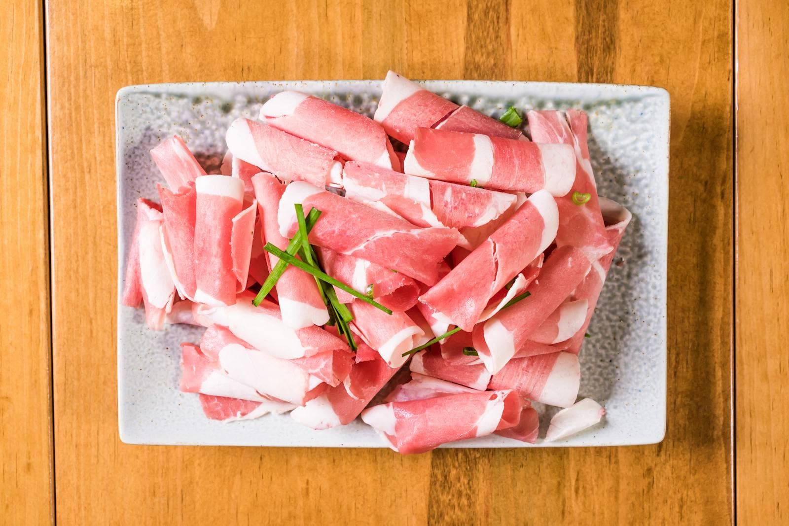 Rolled thin slices of usamgyeop beef belly with white fat striping the red lean, plated with green onion garnish